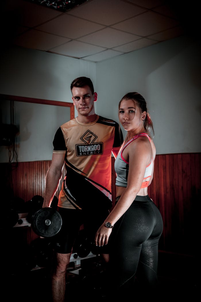 A muscular man and woman posing with dumbbells in a gym setting, showcasing fitness and strength.